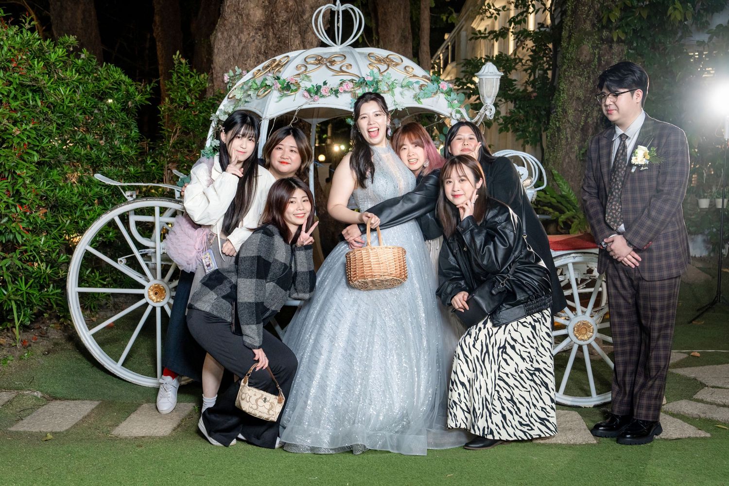 Wedding party poses together for outdoor evening photos with rustic wooden wagon wheel decorations in the background.