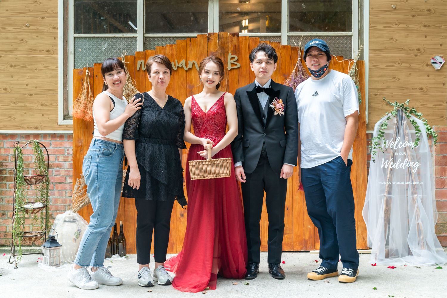 Small group poses in front of orange wooden backdrop with wedding decorations.
