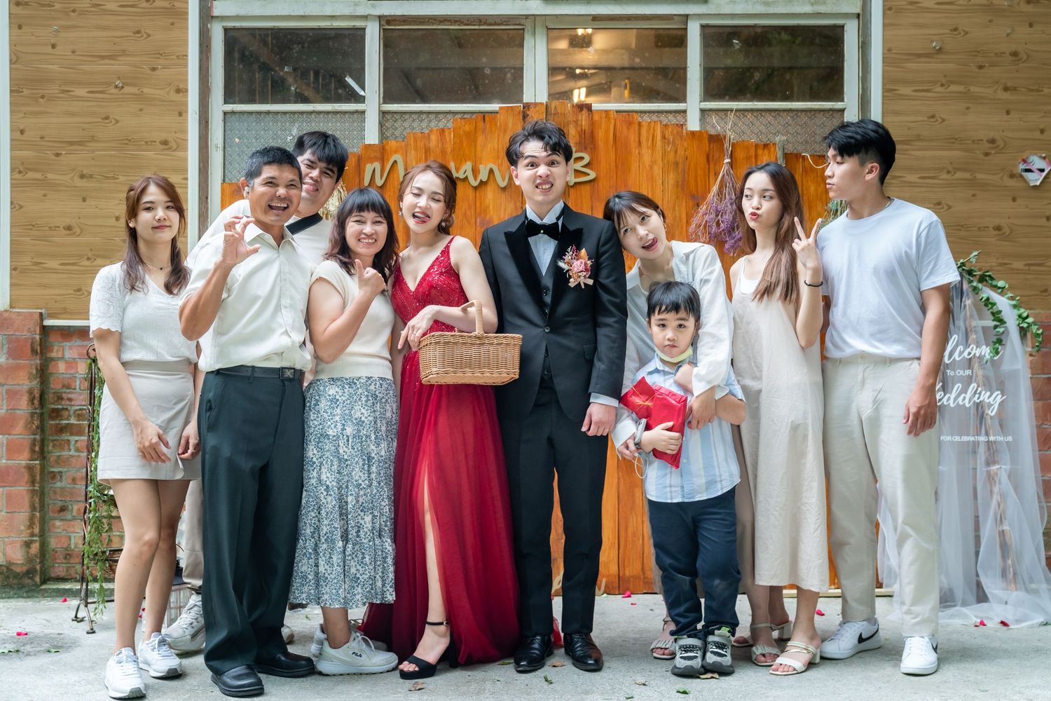 Formal gathering poses together against rustic backdrop with decorative elements and white dress display.