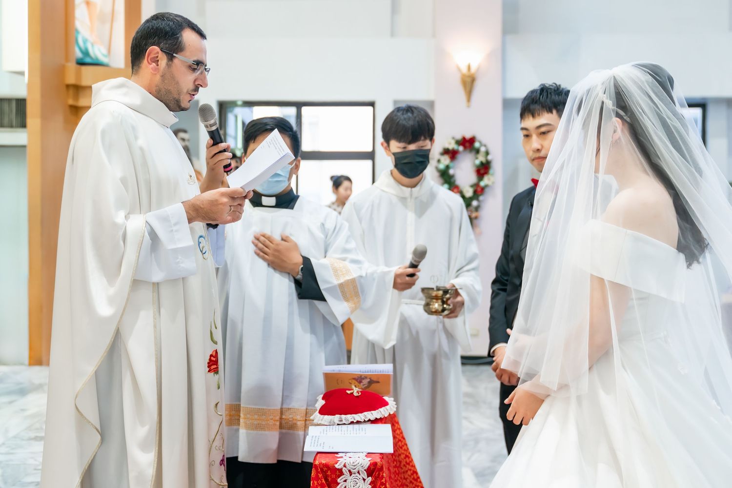 A Catholic wedding ceremony showing the blessing of rings on a red cloth covered table.