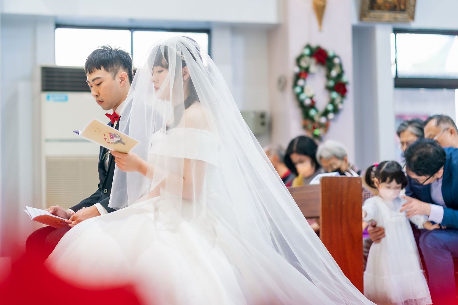 Wedding ceremony in progress with couple seated in church pews.