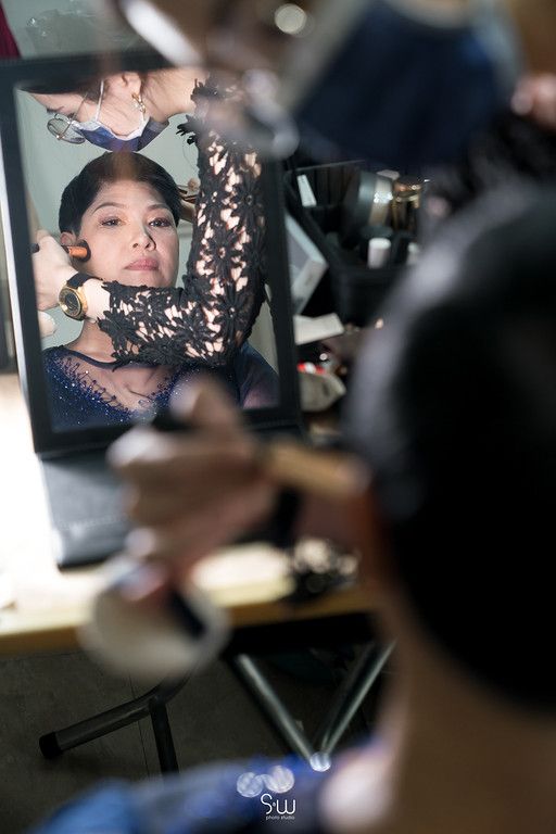 A reflection in a makeup mirror shows someone having their hair styled.