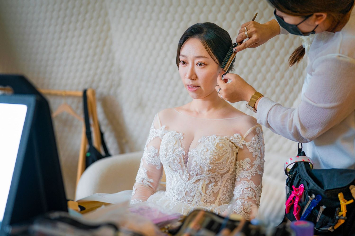 A bride getting ready for her wedding with lace details on her wedding gown visible in the getting-ready room.