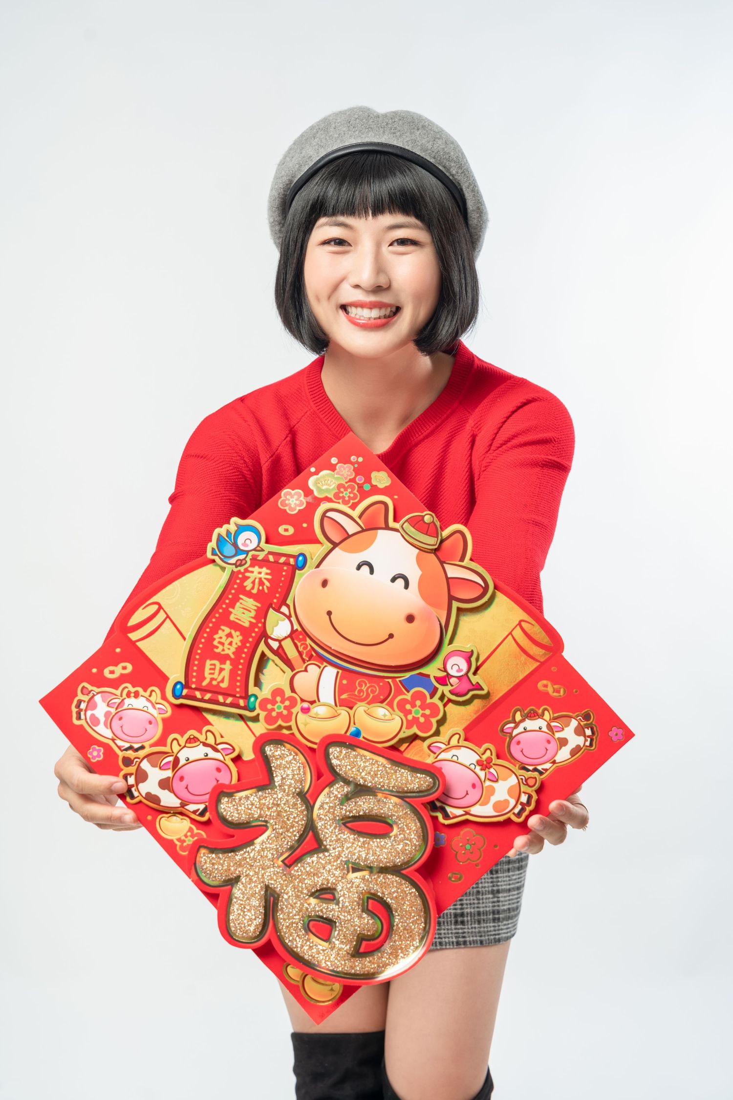 Person wearing red sweater and grey cap holds festive Chinese New Year decorations with cartoon ox and fu character designs.