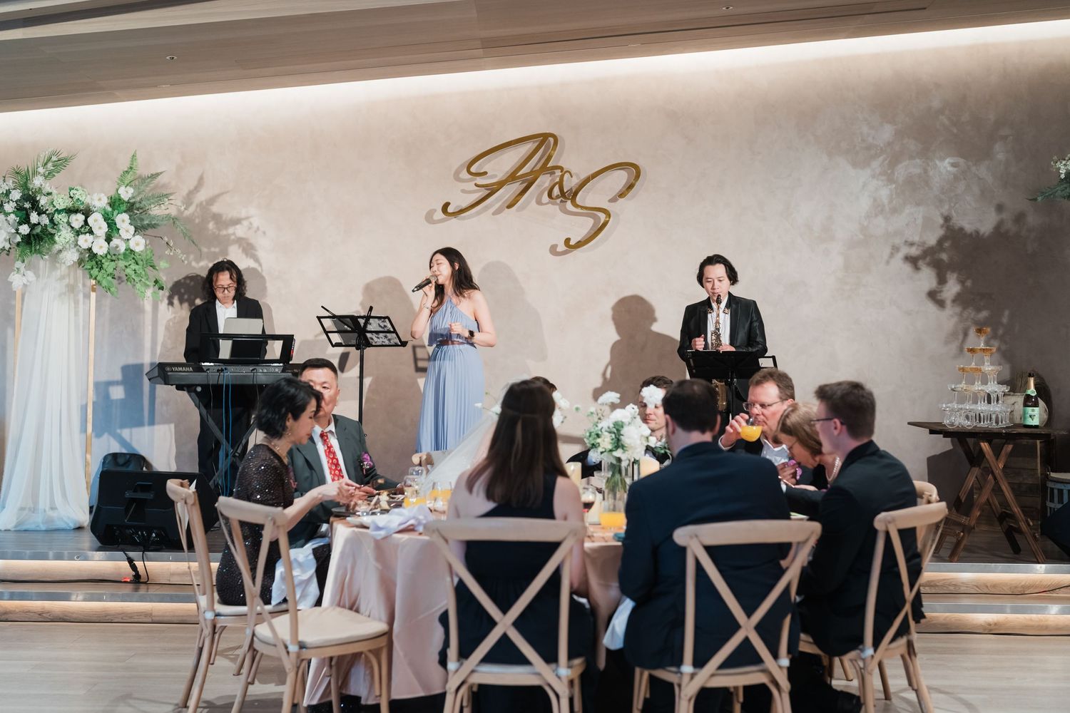 Elegant wedding reception dinner party with guests seated at decorated tables while musicians perform on stage.