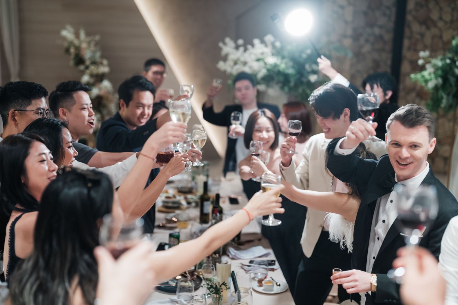 Wedding guests raise their glasses in celebration during a joyful toast at an elegant reception.