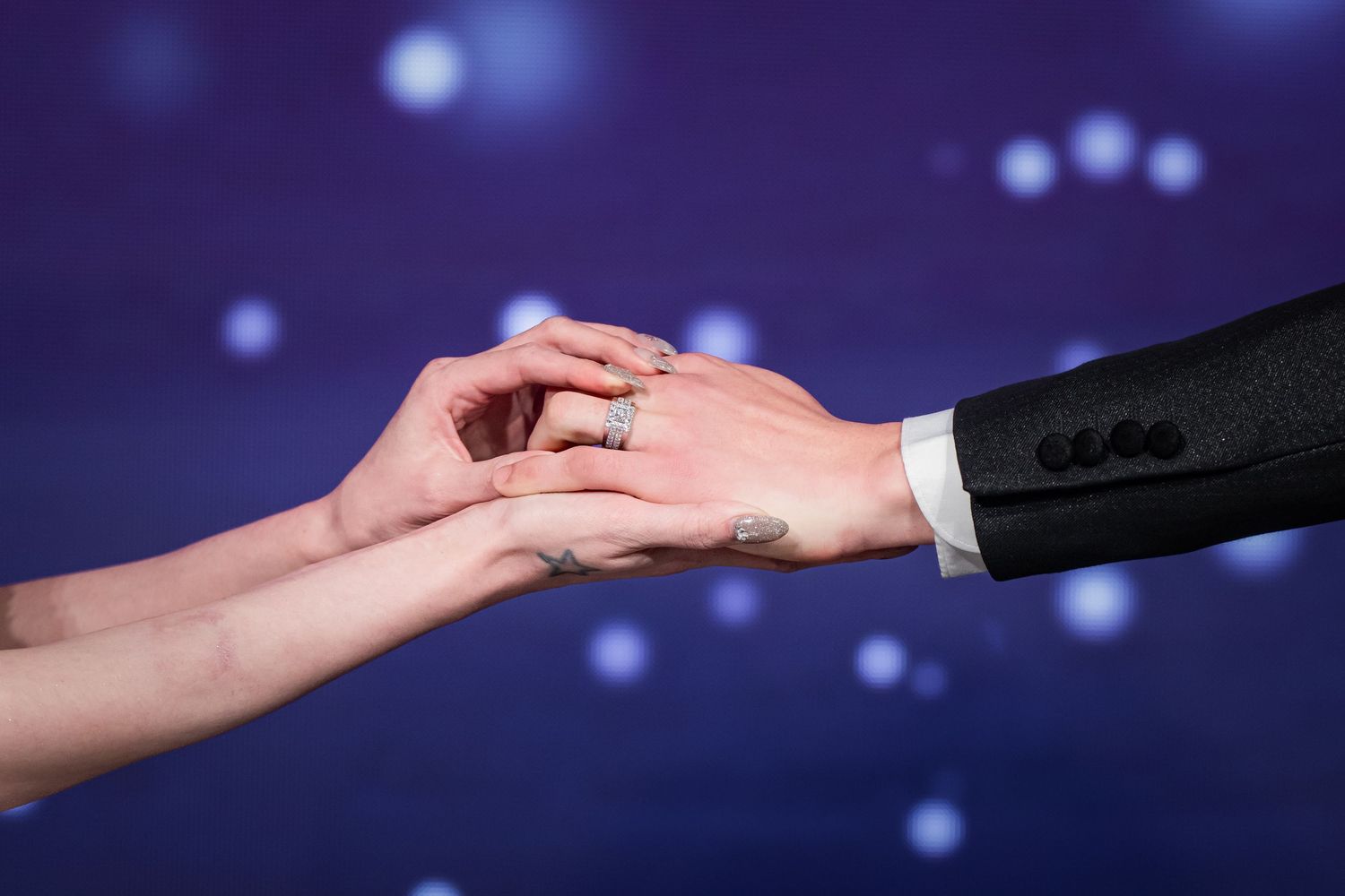 Two hands reaching towards each other against a dark blue background with bokeh light effects.