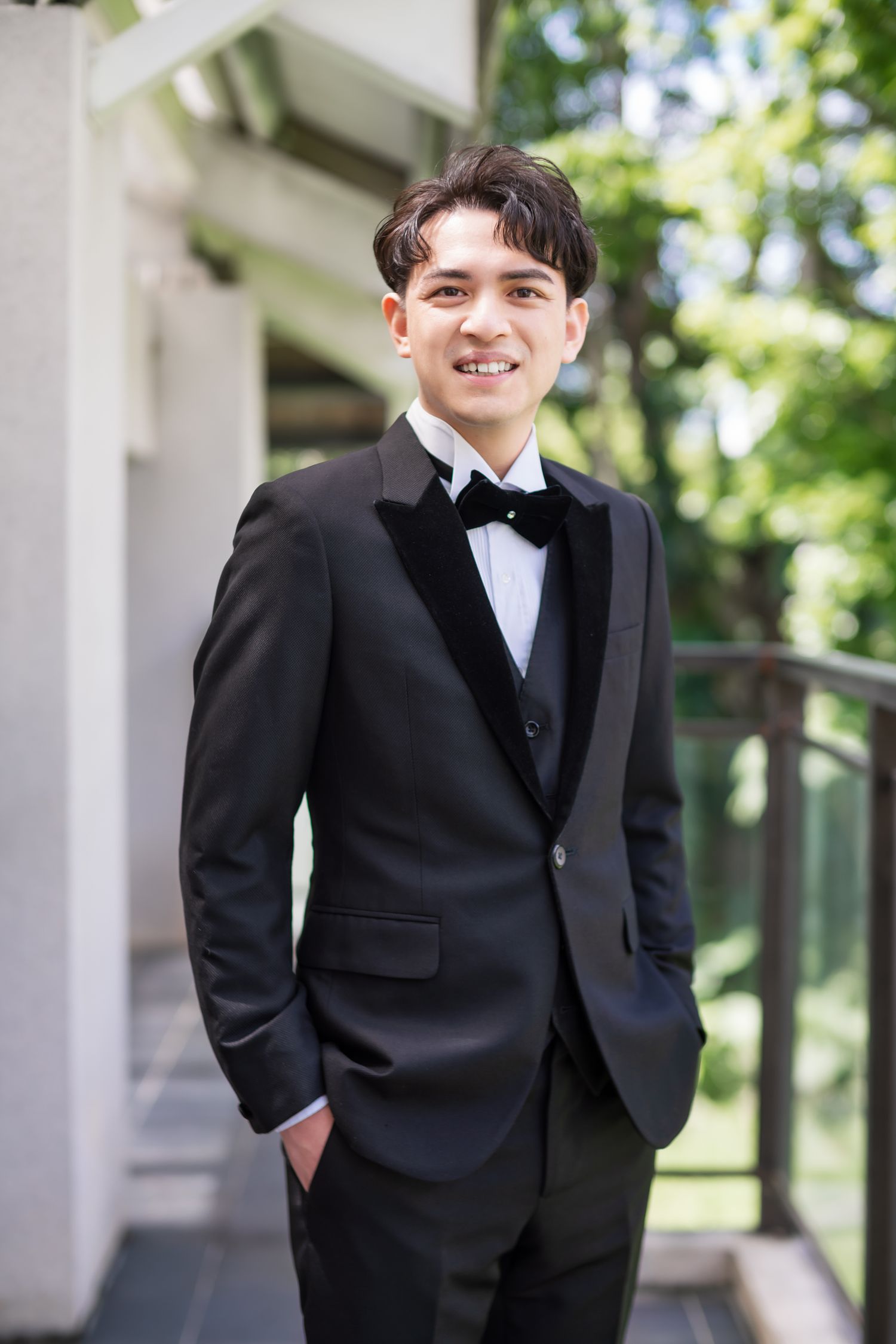 Groom in fitted black tuxedo smiling on outdoor terrace.