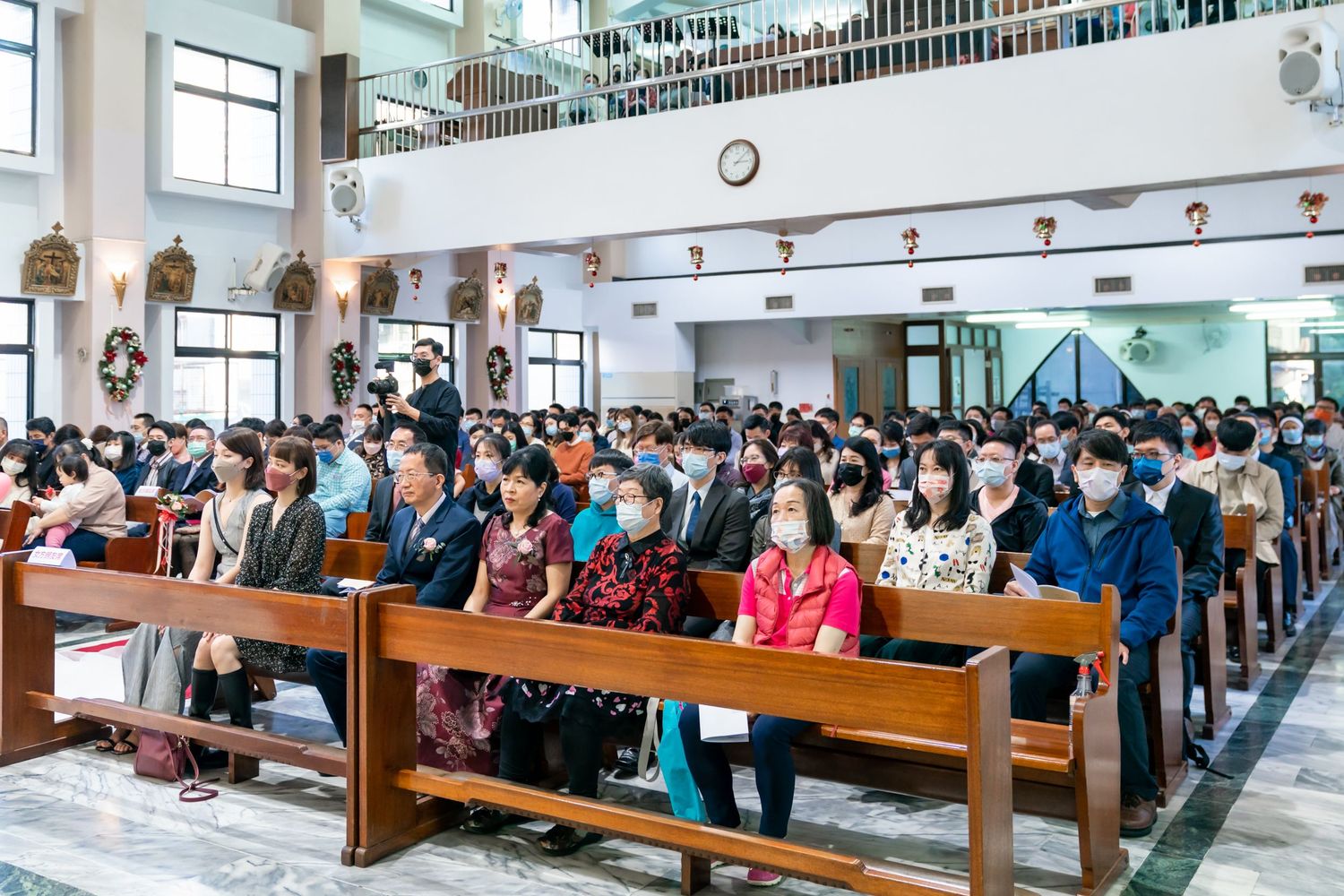 A large congregation gathers in a church with wooden pews and a balcony level.