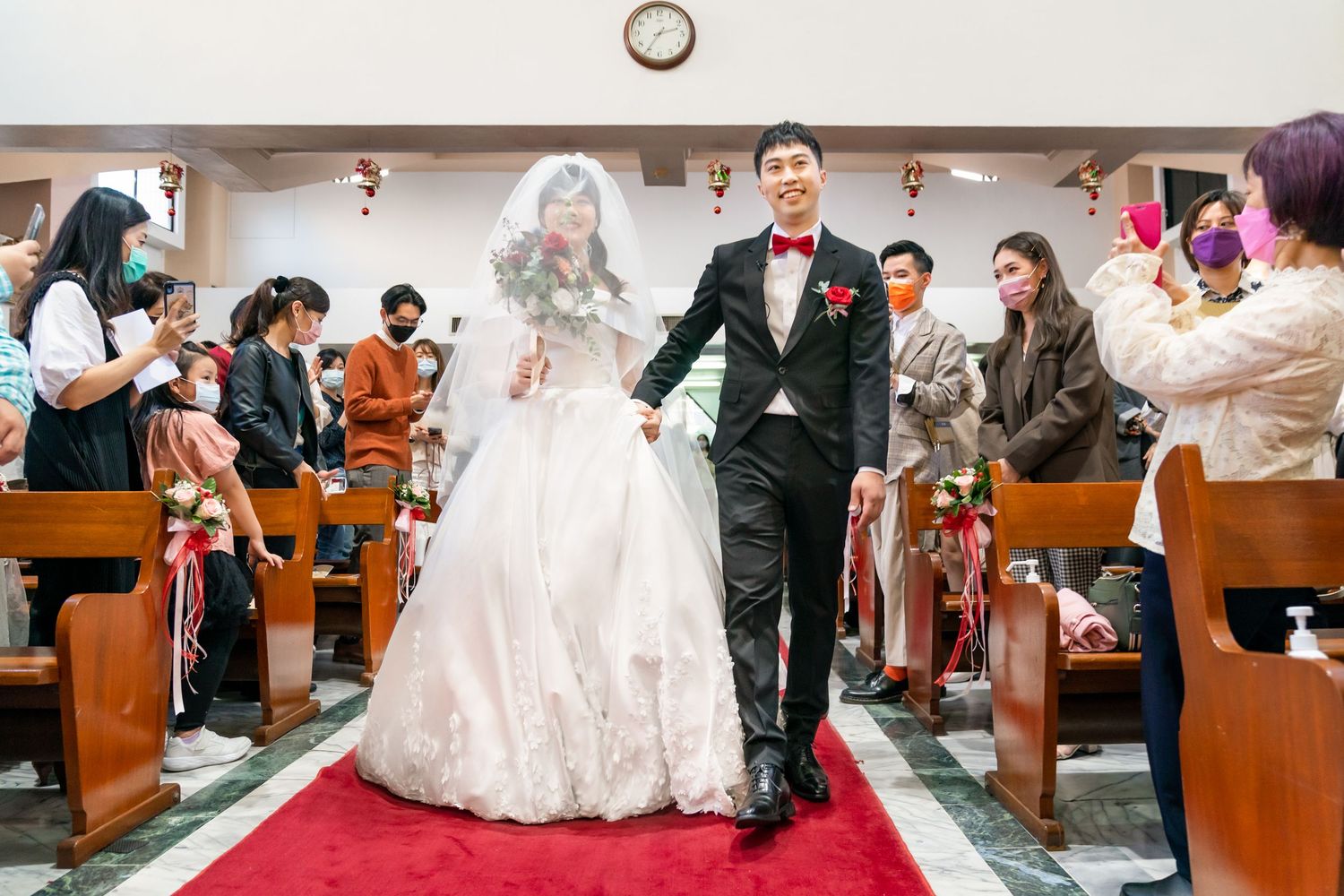 Newlyweds walking down church aisle after ceremony while guests capture photos.