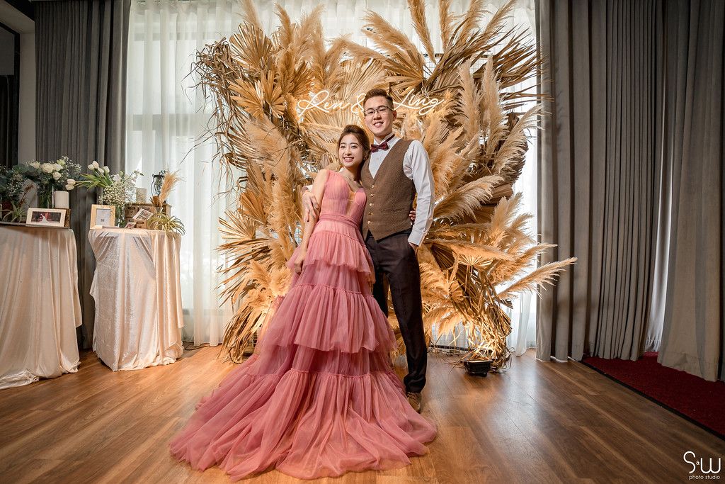 A couple poses in front of dramatic dried palm leaf wedding backdrop.