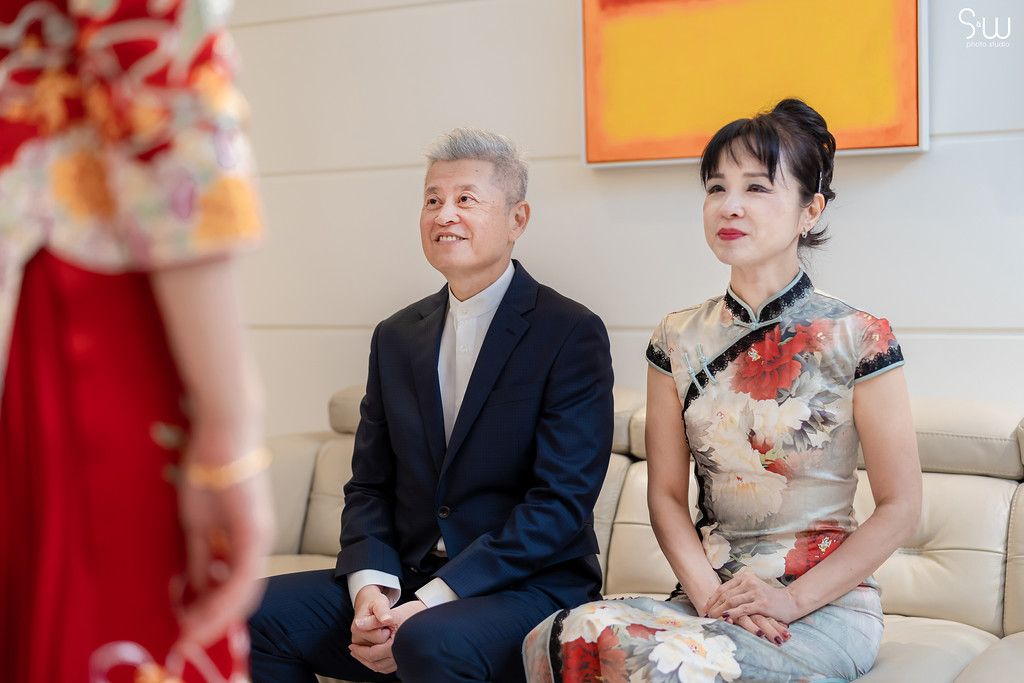 Traditional Chinese wedding scene with guests in formal attire and cheongsam dress seated on couch.