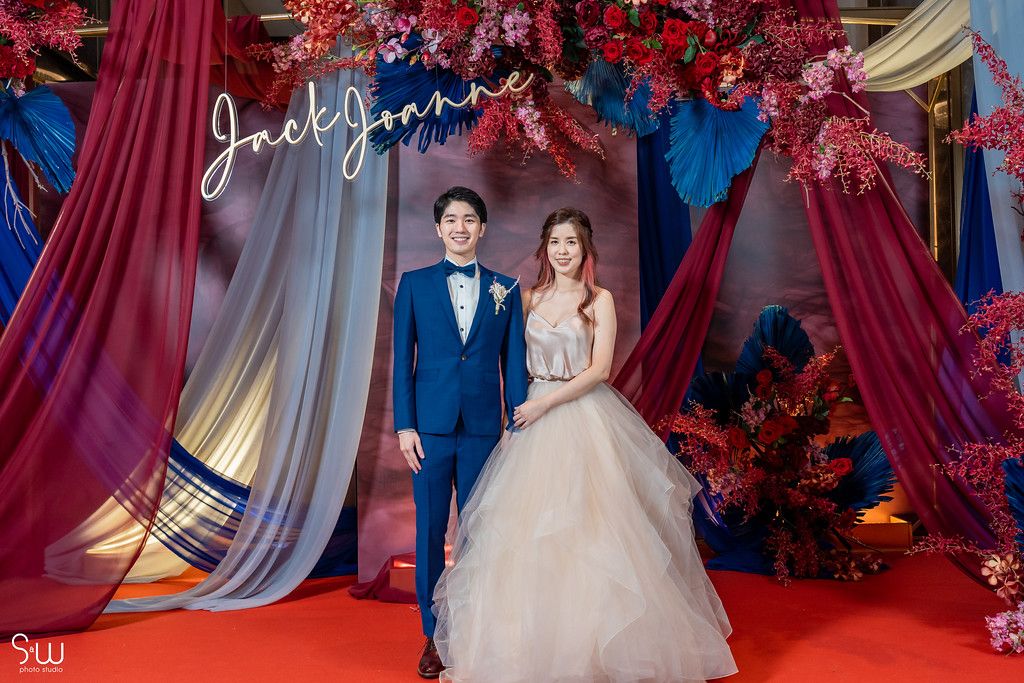 Classic wedding portrait on red carpet with dramatic floral arch and draped backdrop.