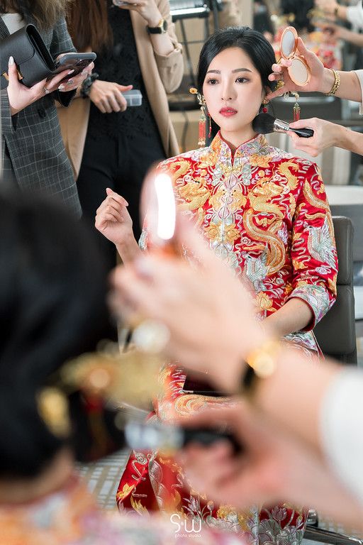 Preparation scene of traditional Chinese wedding with stylists doing hair and makeup in red qipao dress.