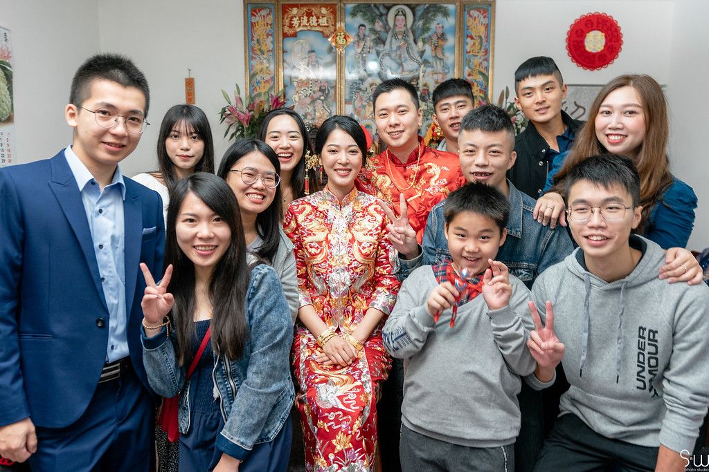 Wedding celebration group photo with traditional Chinese decor and red qipao dress.