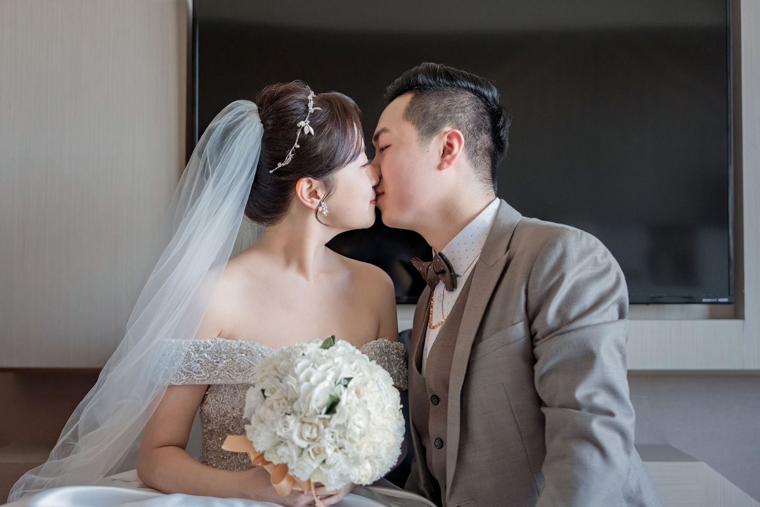 A romantic wedding couple shares a tender kiss while holding a white bouquet of flowers during their special day.