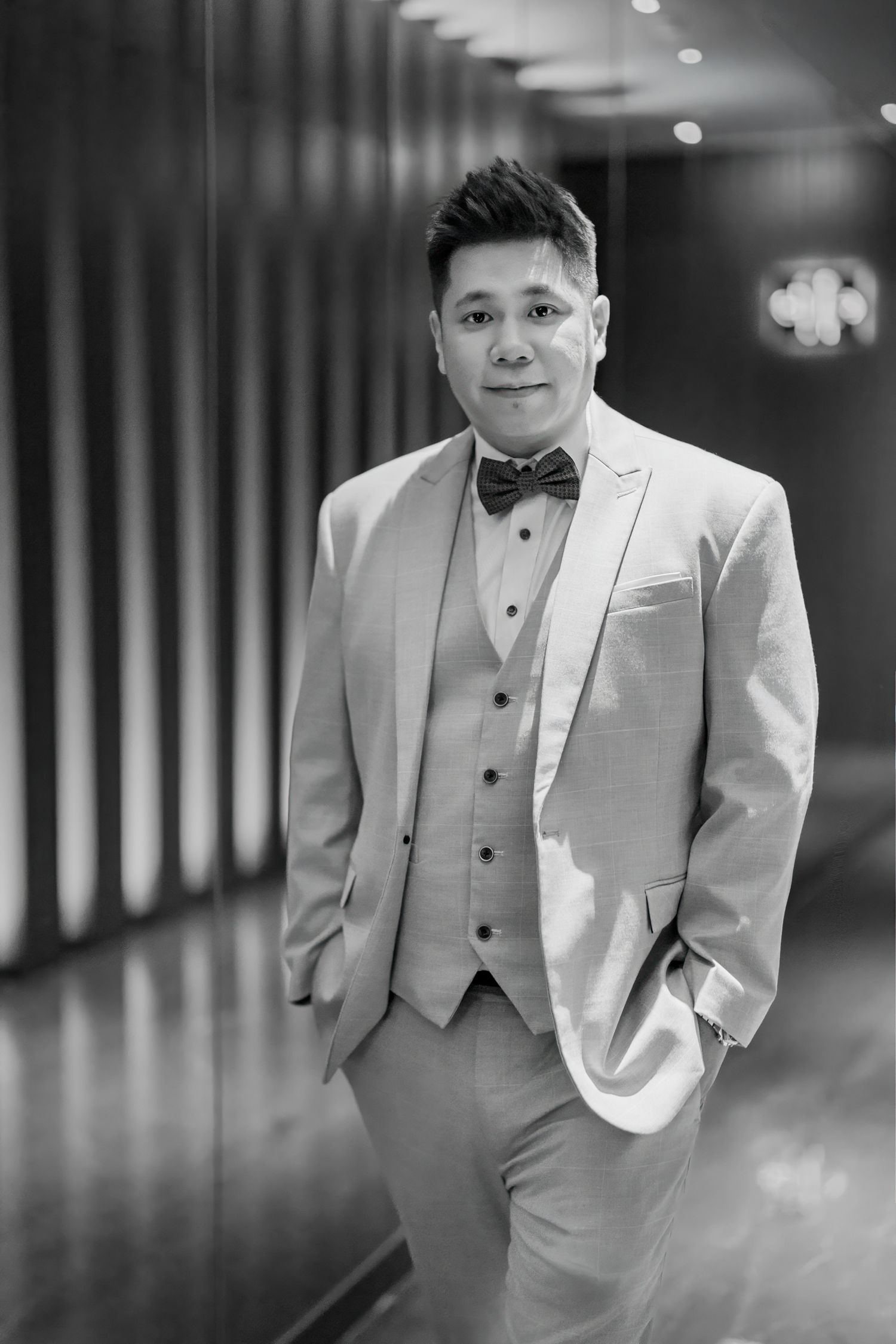 Black and white portrait photos of a person wearing a light colored formal suit and vest in a dimly lit hallway.