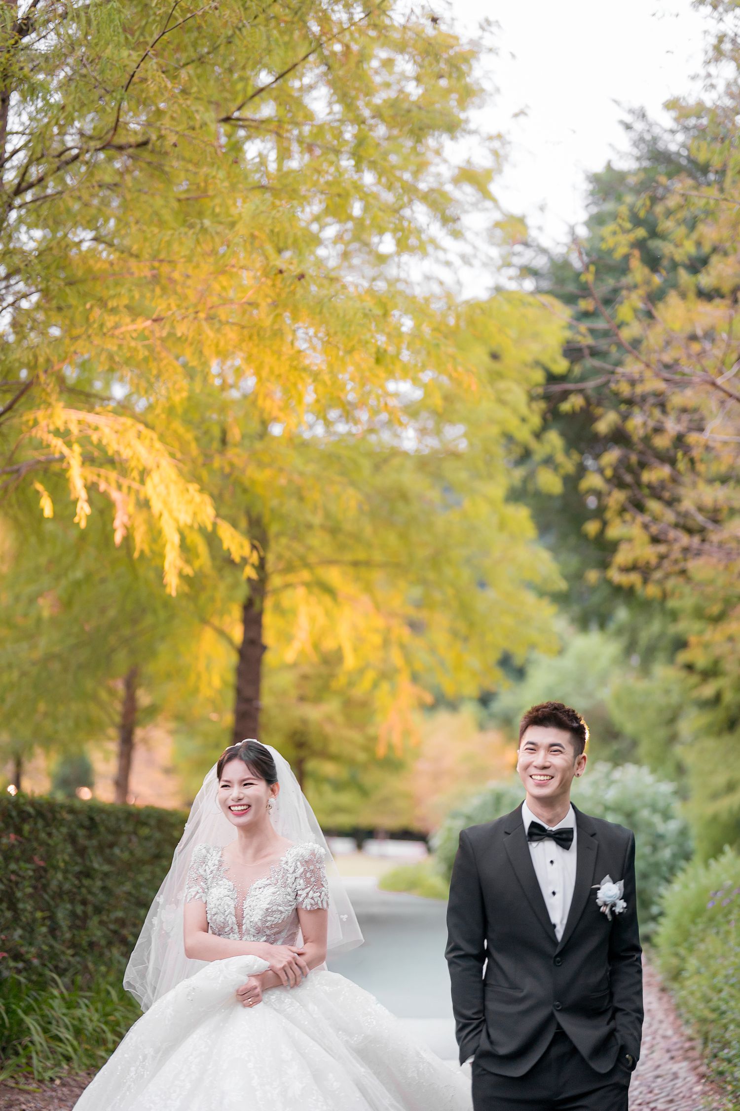 A couple shares a joyful moment together on a tree-lined path during an autumn wedding photoshoot.