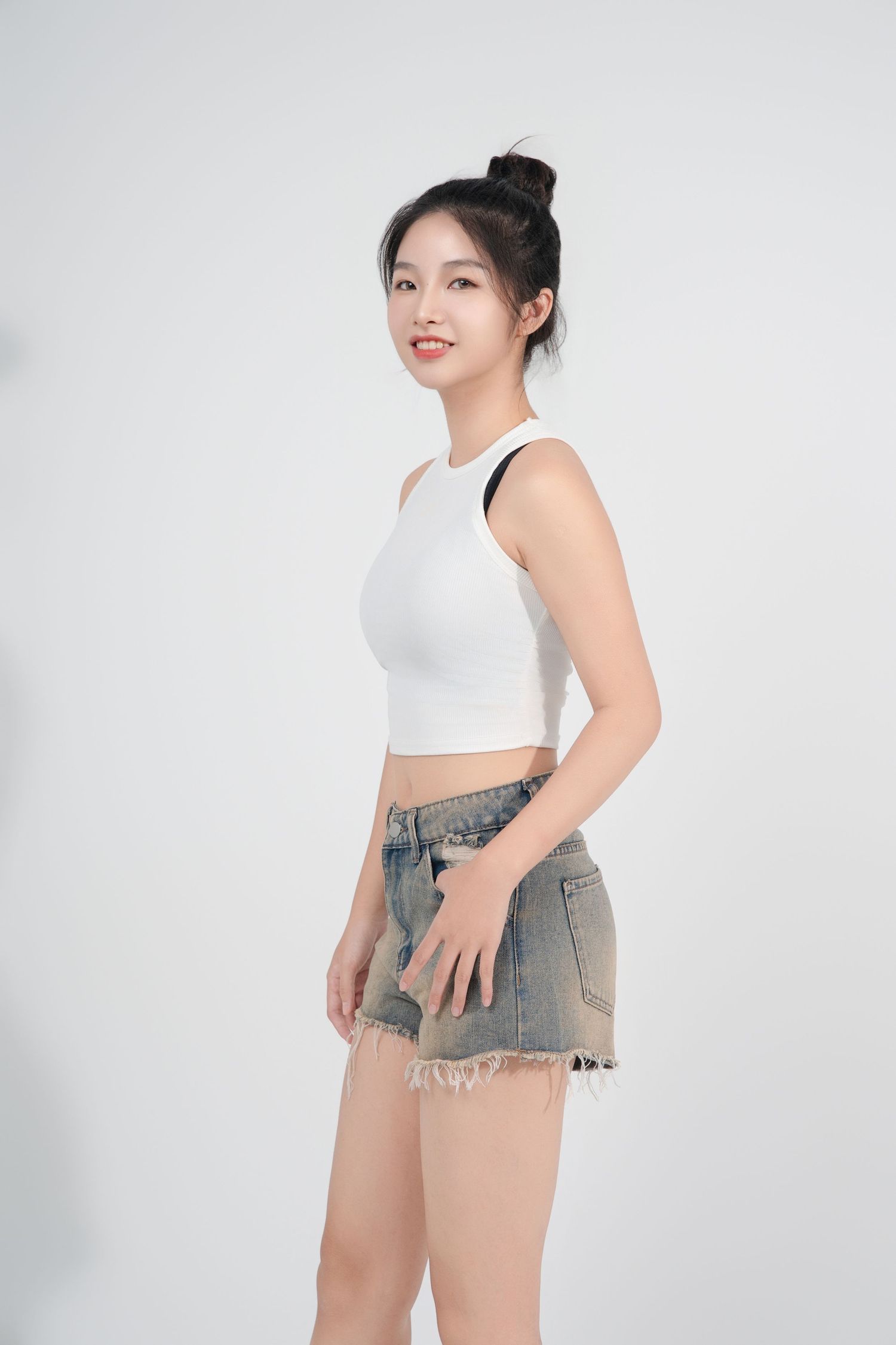 A model wearing a white crop top and denim shorts poses against a white background in a fashion photography series.