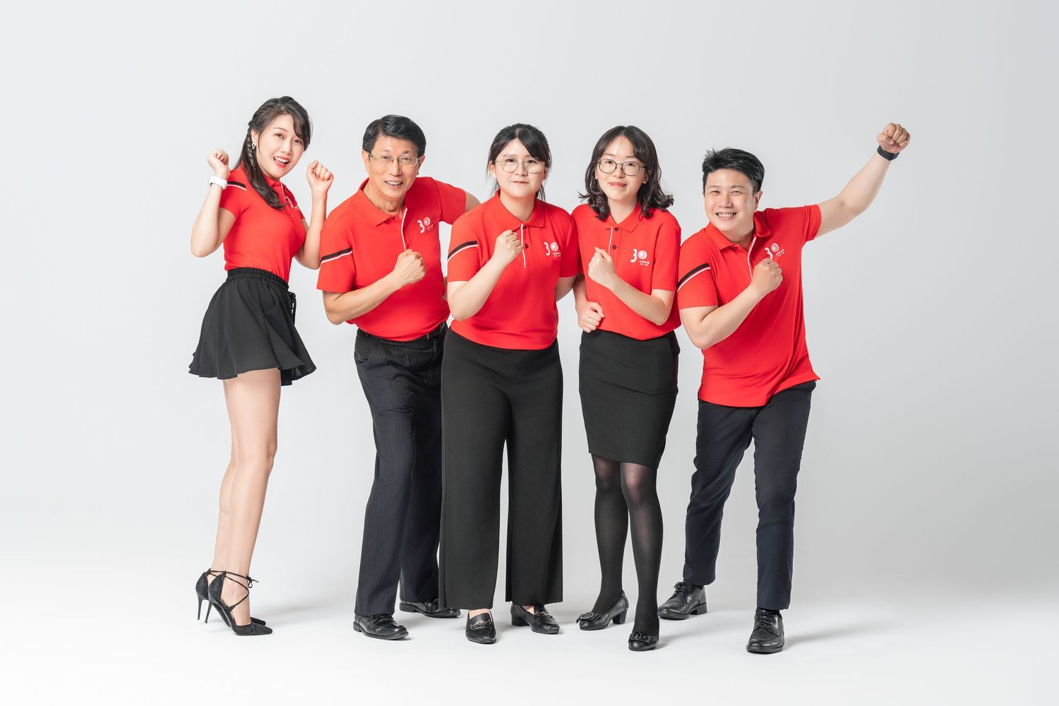 A group of people wearing red shirts and black pants pose together against a white background.