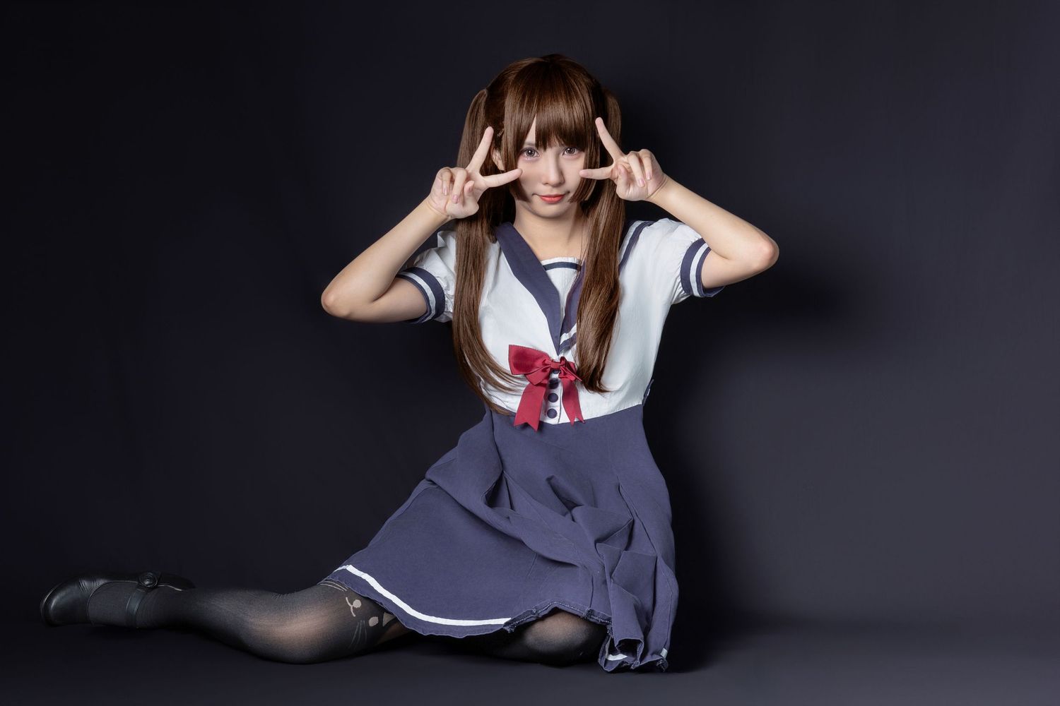 A person in a Japanese school uniform with sailor collar and navy skirt poses playfully against a dark background.