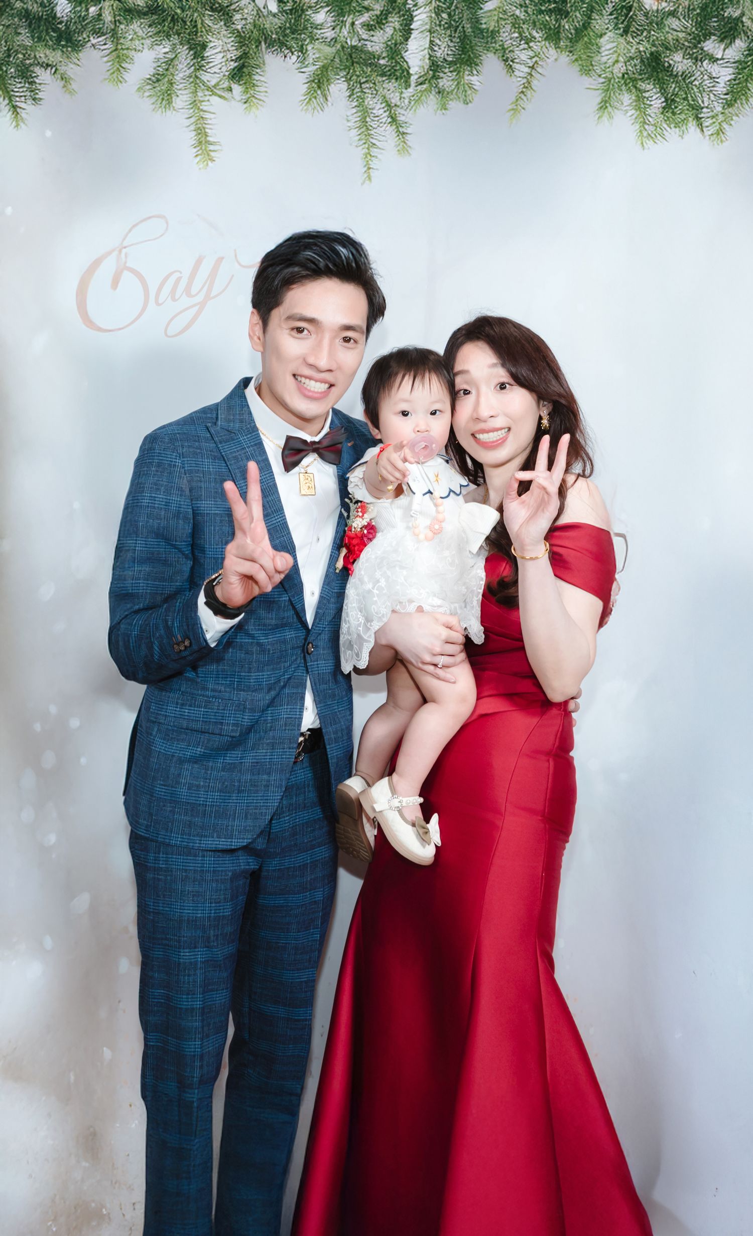 A family portrait against a light background with evergreen branches, featuring formal attire in navy blue and deep red.