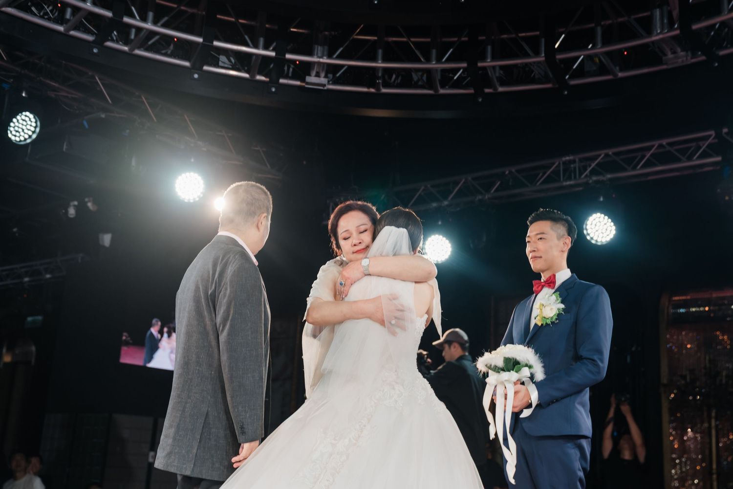 A wedding ceremony taking place on a dimly lit stage with spotlights illuminating the scene.
