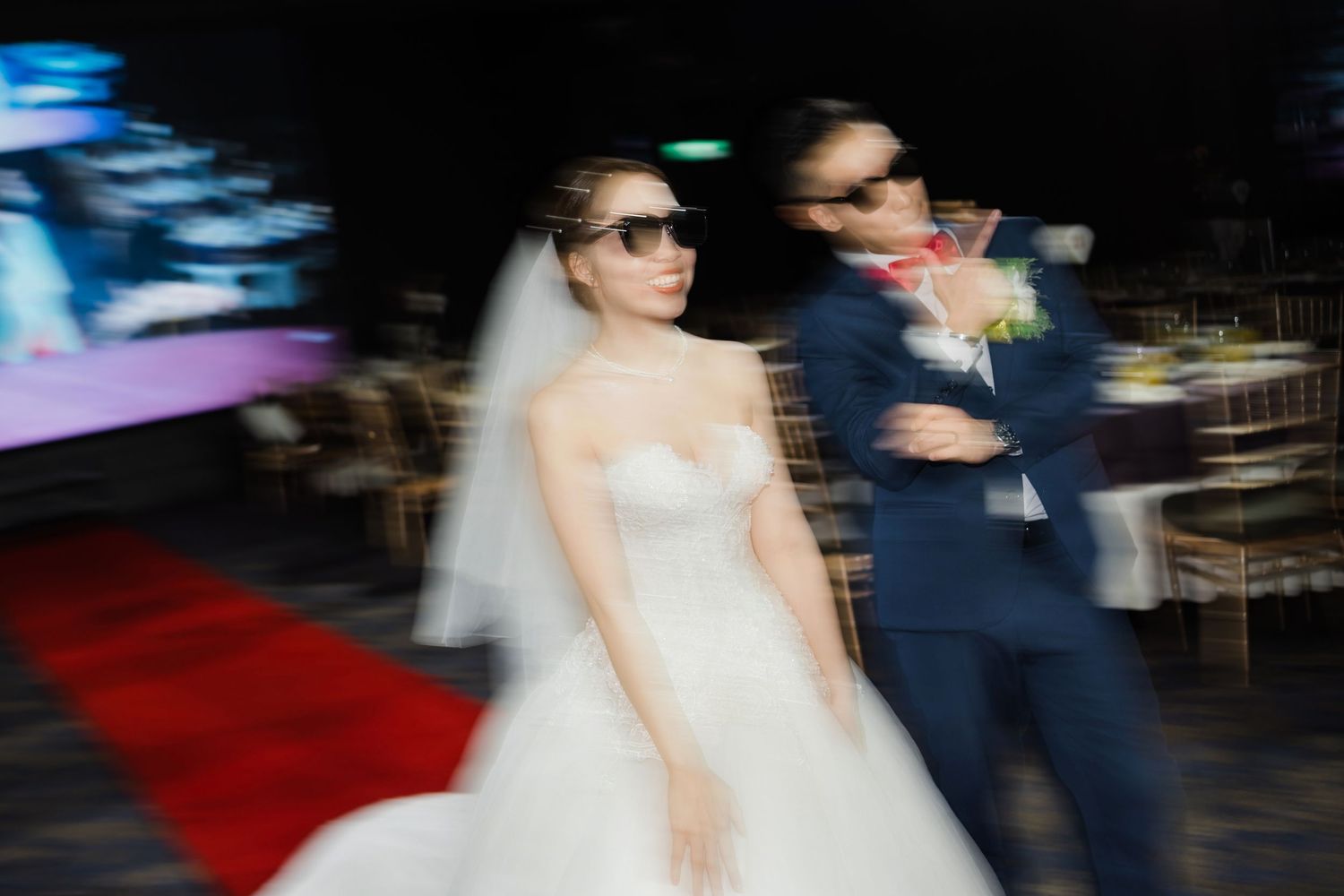 Motion blur photo of a bride and groom walking quickly down a red carpet at their wedding ceremony.