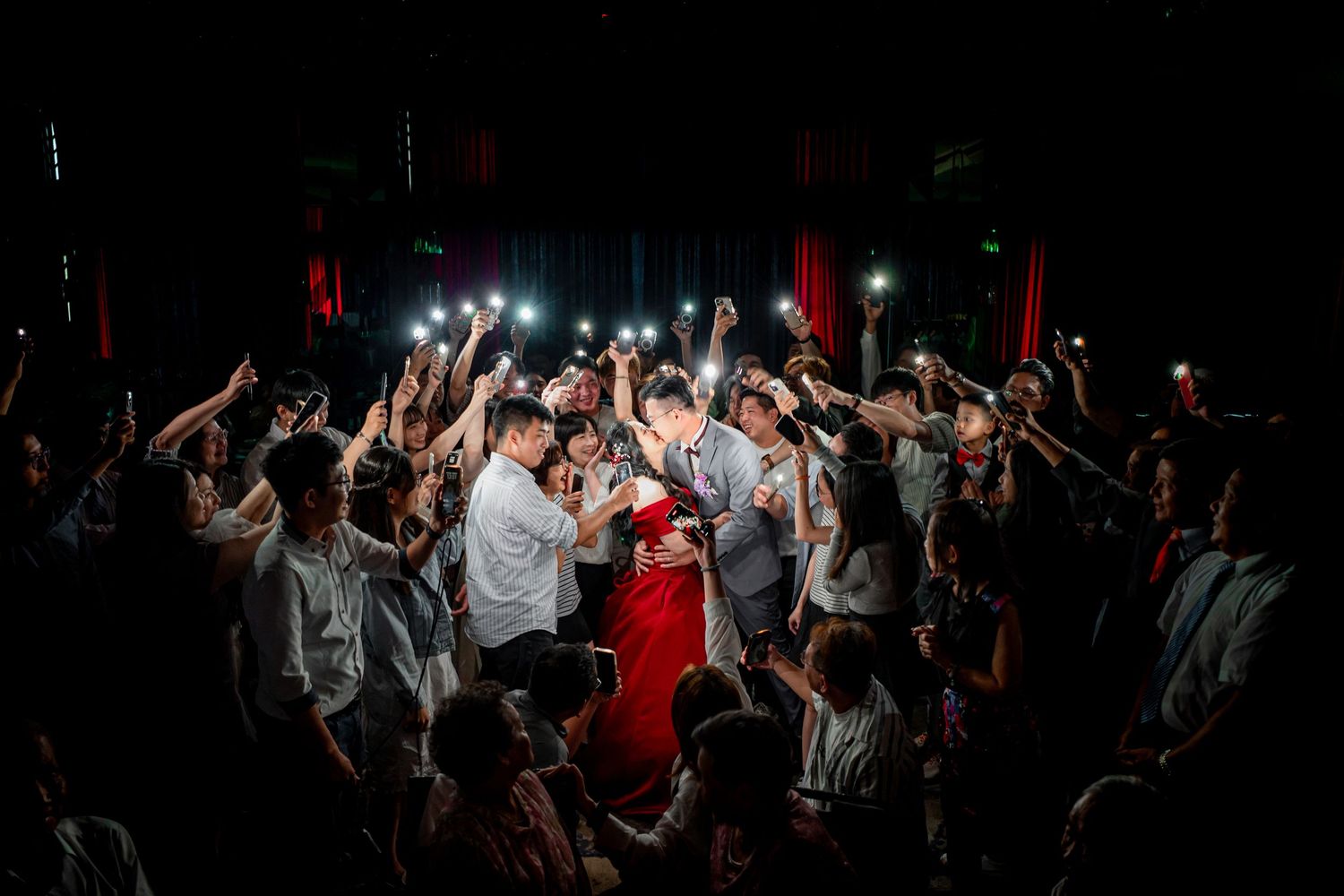 A crowd of energetic dancers surrounds a person wearing red in a dark nightclub atmosphere illuminated by spotlights.