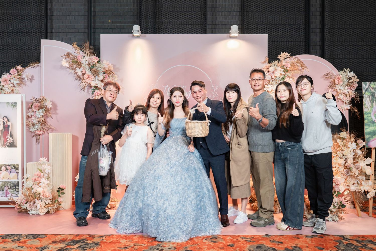 A group of people posing at a formal event with pink floral decorations and a light blue gown in view.