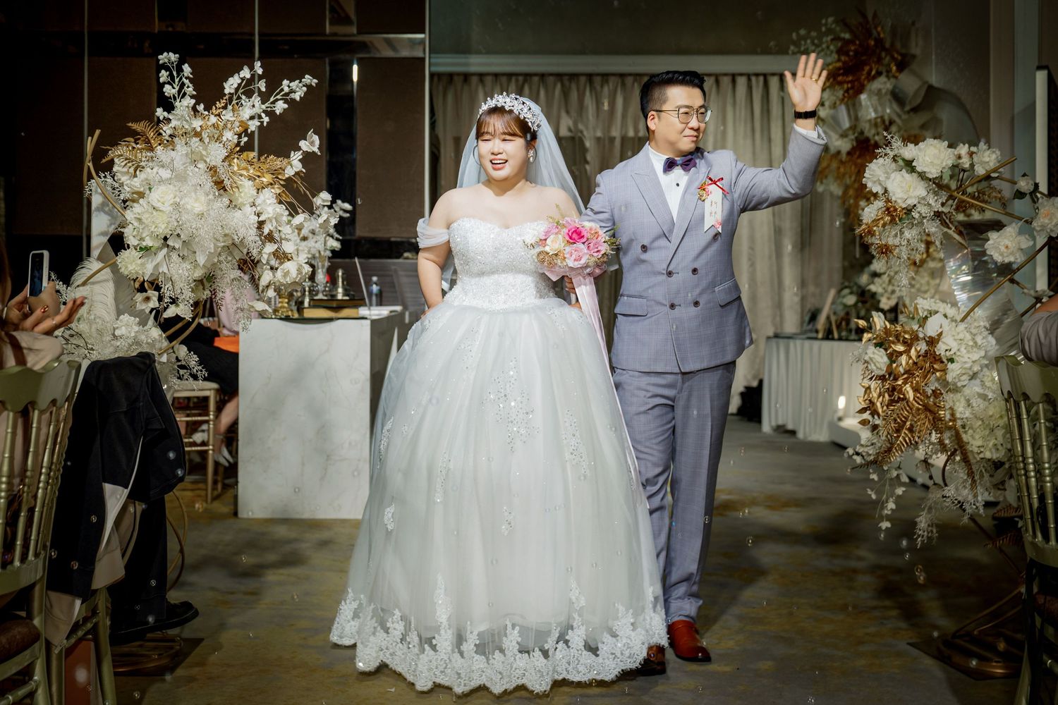 A wedding couple stands together in a beautifully decorated venue with floral arrangements and elegant decor.