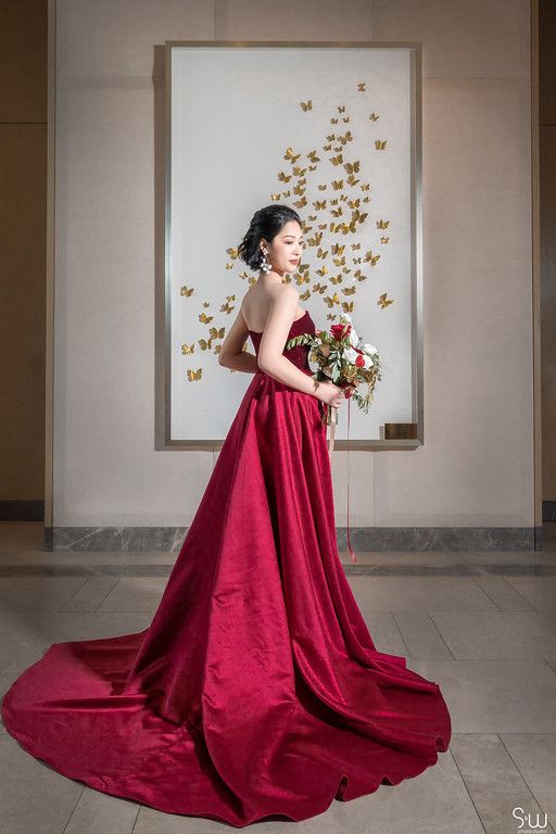Side profile of bride in dramatic red gown with long train against butterfly wall art.