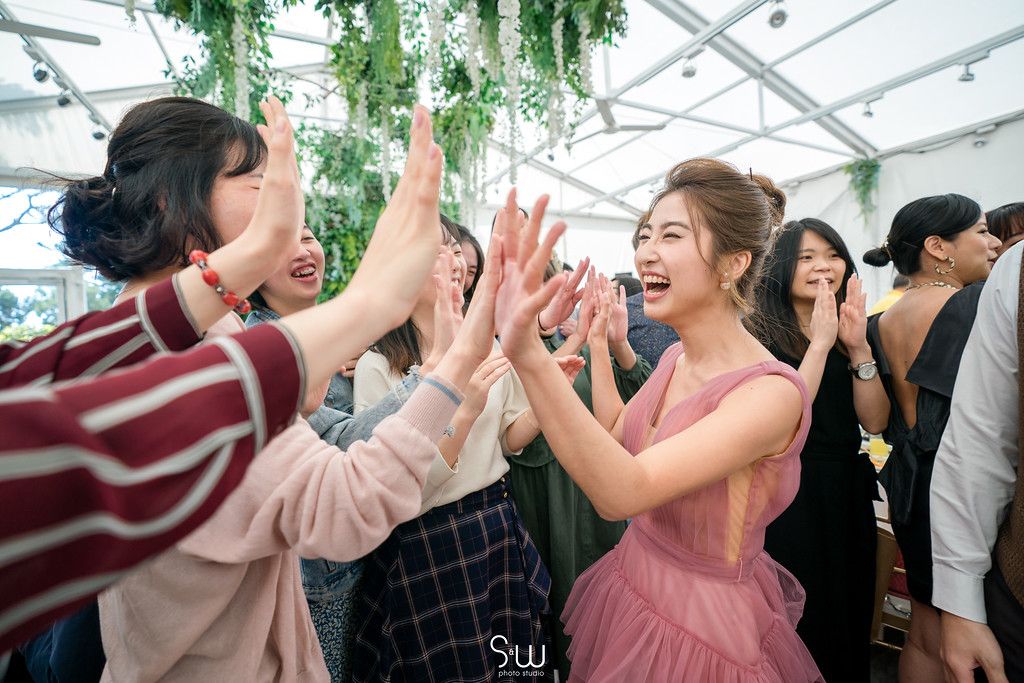 Joyful celebration with guests high-fiving and cheering under hanging greenery at an indoor venue.