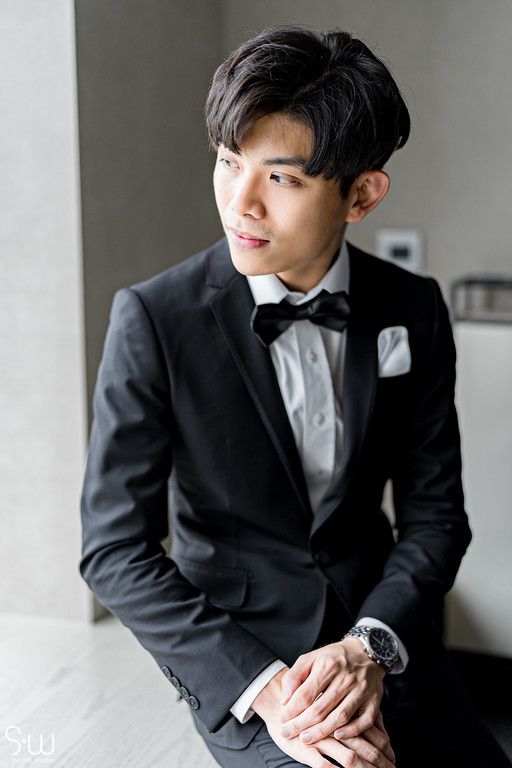 A groom in a black tuxedo and bow tie looks off to the side in a formal portrait.