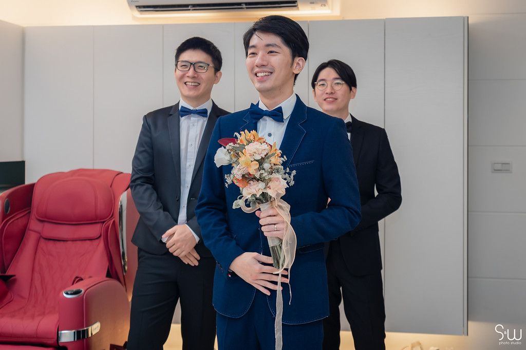 Groomsmen in formal suits sharing laughs while holding a floral bouquet.