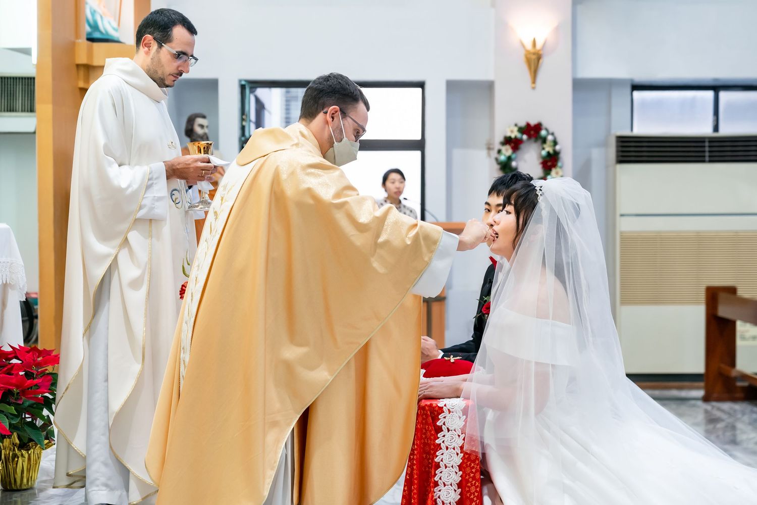 Ceremonial blessing during Catholic wedding with priests in white and gold vestments at church altar.