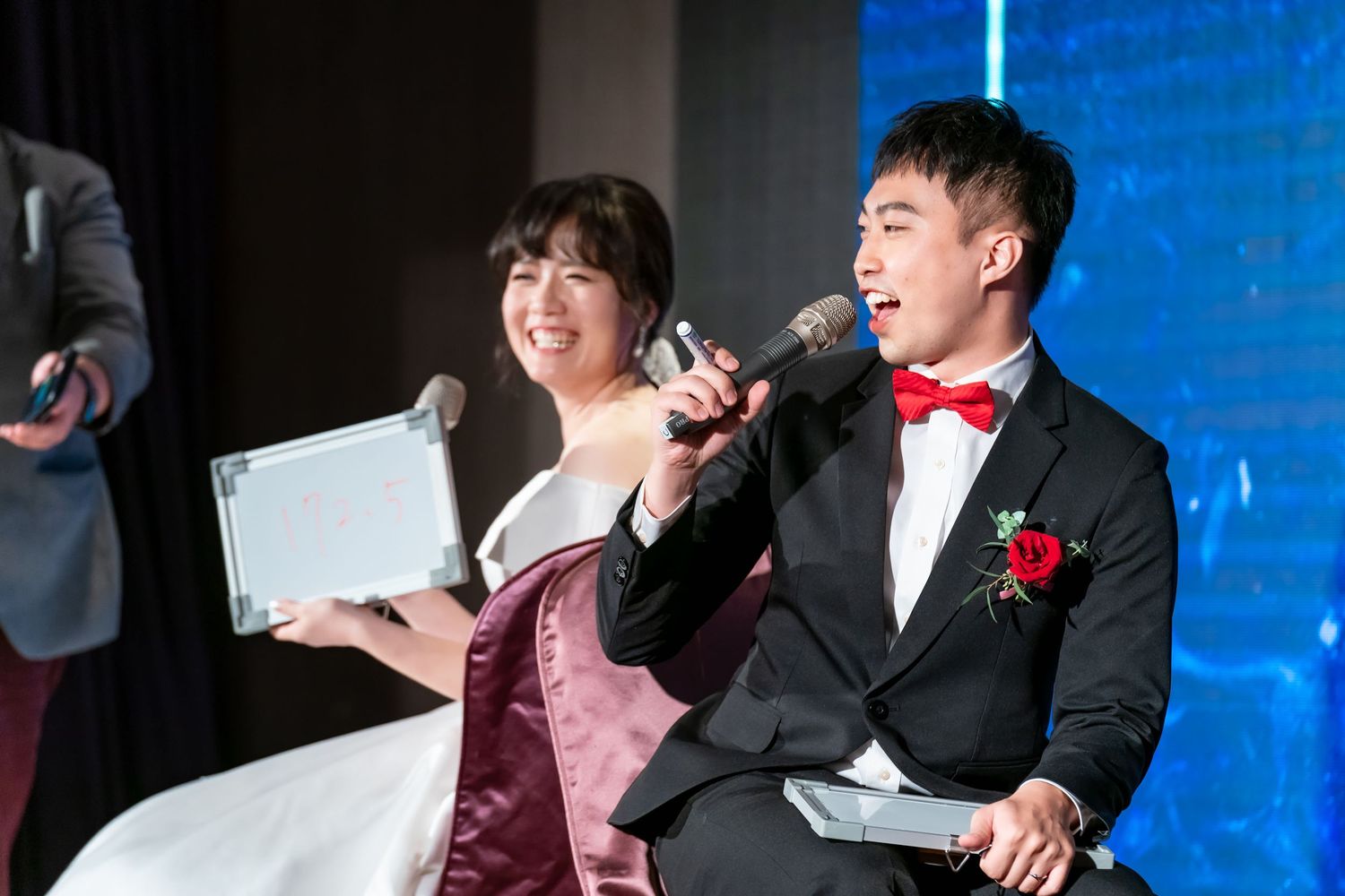 Wedding couple sits on stage with microphones participating in a reception game.
