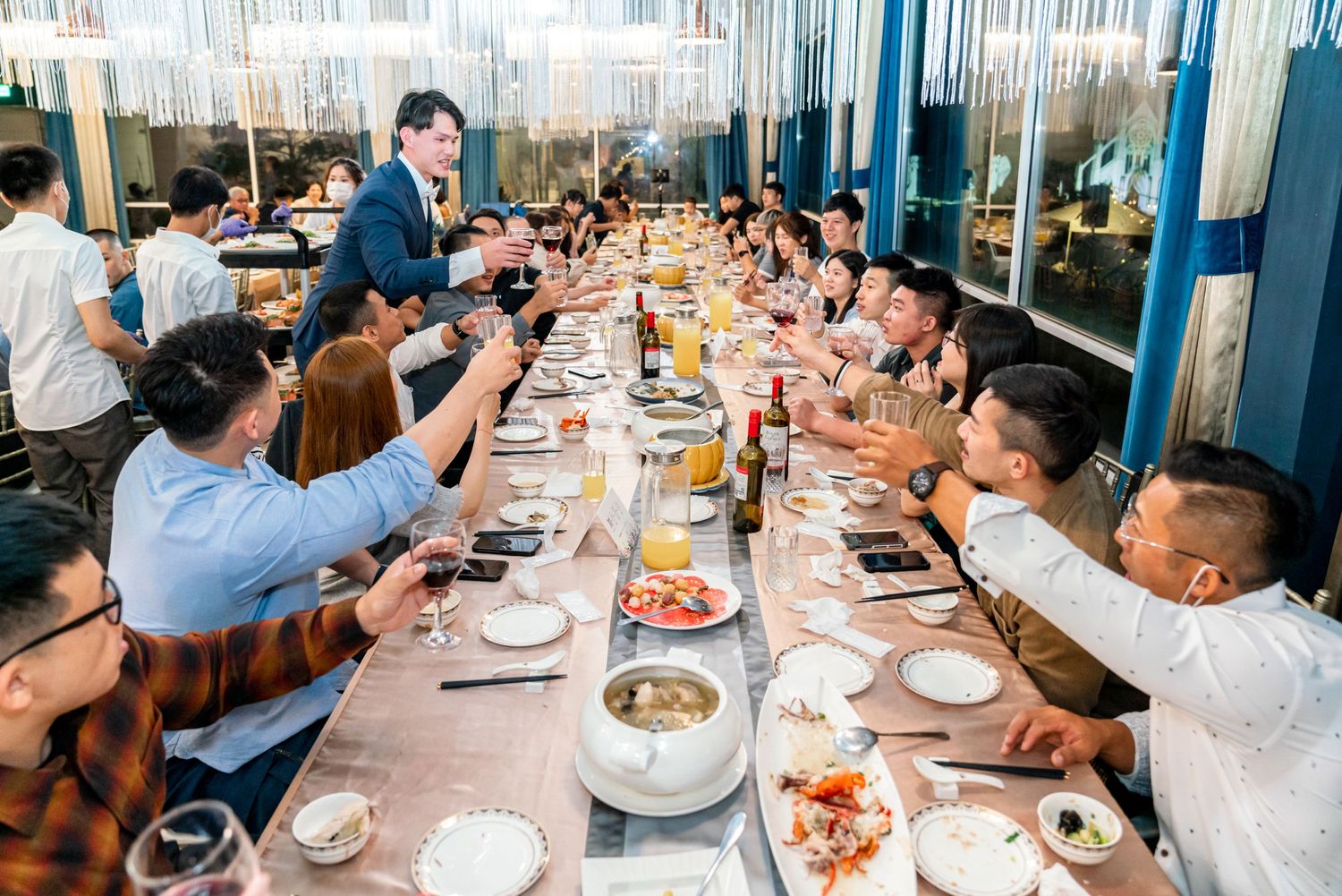 A group of people raise glasses in a toast during a celebratory dinner at a restaurant with blue decor.
