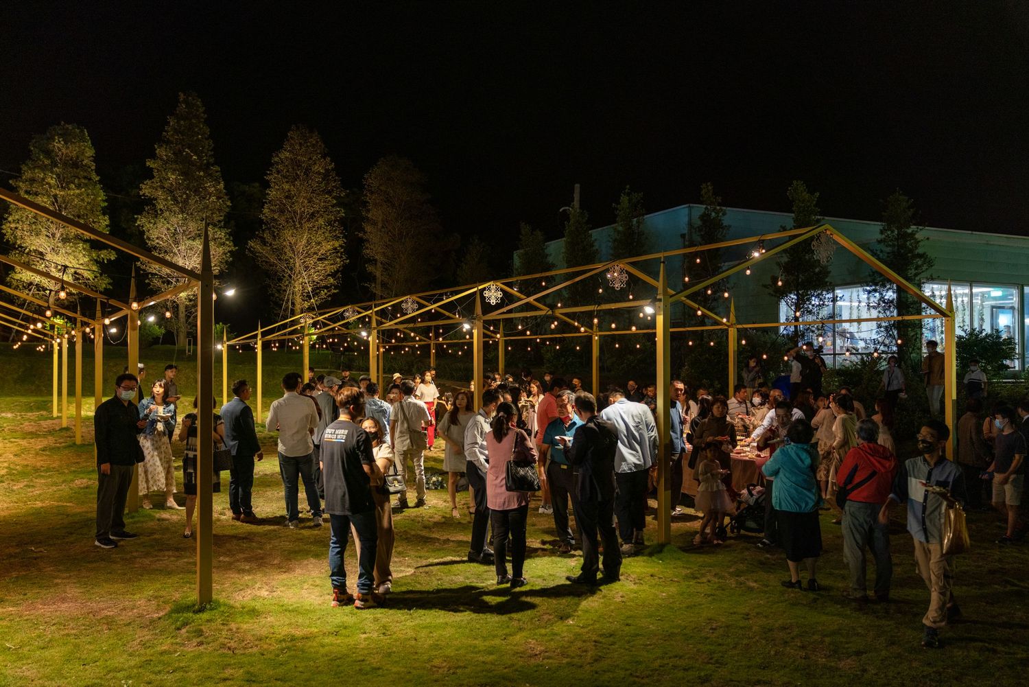 Guests gather under string lights at an outdoor evening wedding reception venue surrounded by illuminated trees.