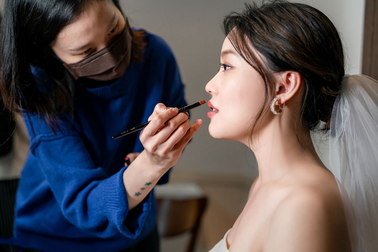 Professional makeup artist in blue sweater applies lipstick to client during bridal preparation session.