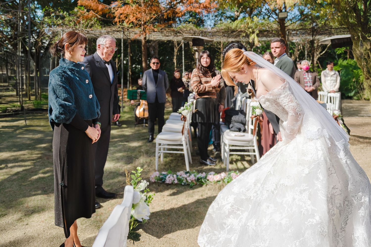 A beautiful outdoor autumn wedding ceremony in a park with guests seated on white chairs and fall foliage in the background.