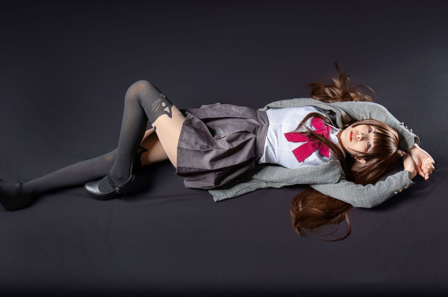 A person wearing a gray skirt and sweater outfit with pink bow lies on a dark surface with hair spread out.