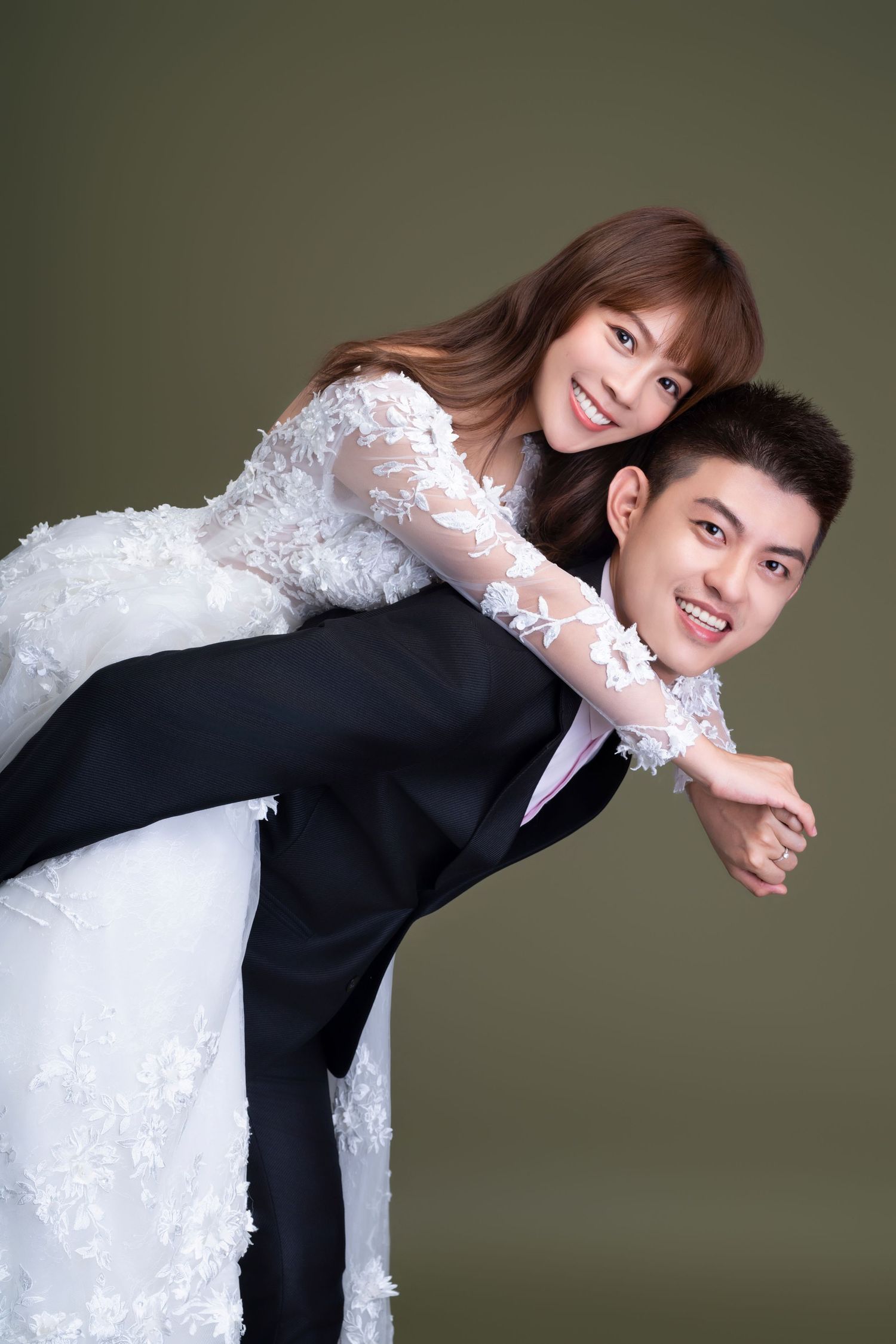 A joyful couple poses playfully in wedding attire against a gray studio backdrop.