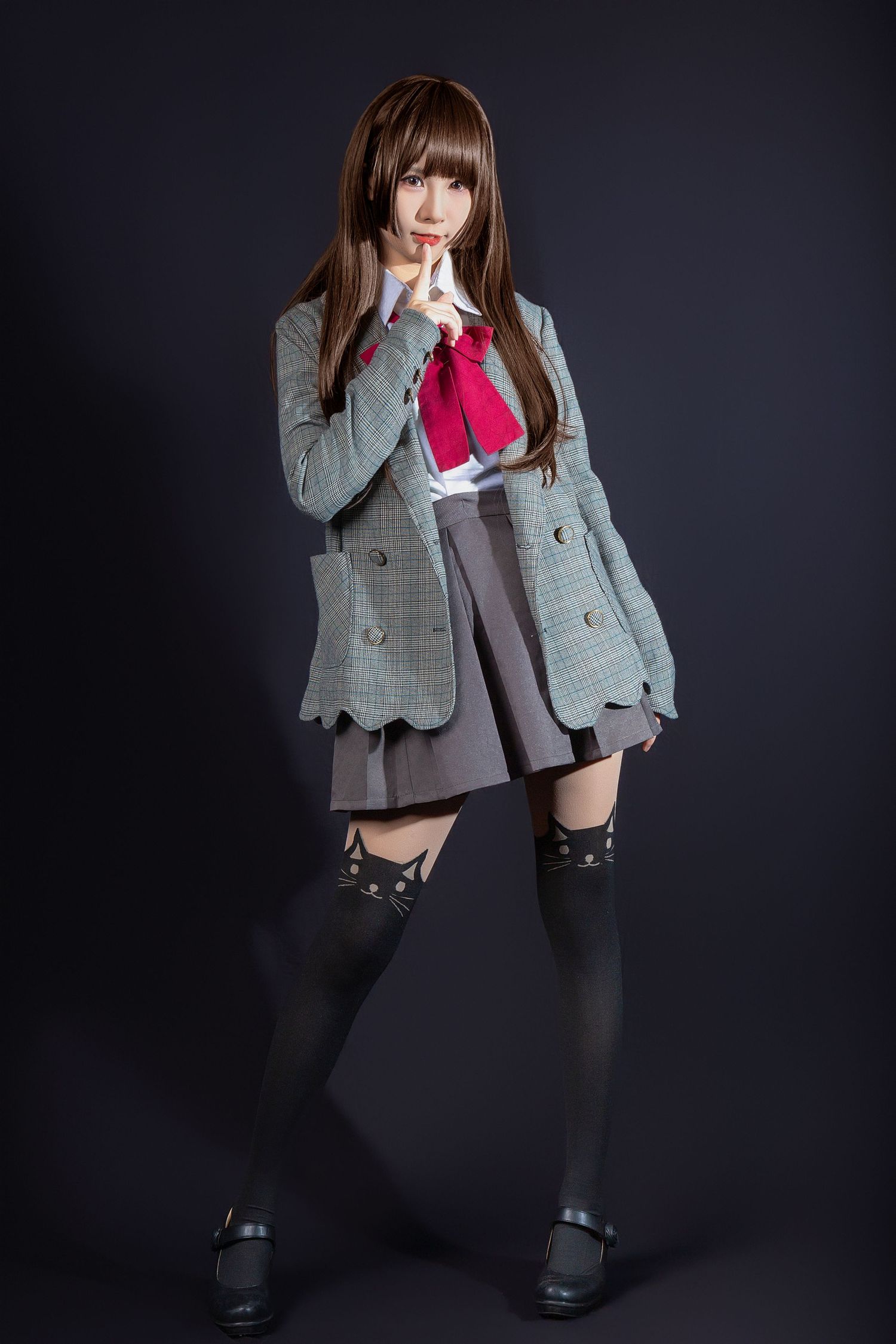 A person in a school uniform style outfit with plaid blazer, skirt, and knee-high socks poses against a dark background.