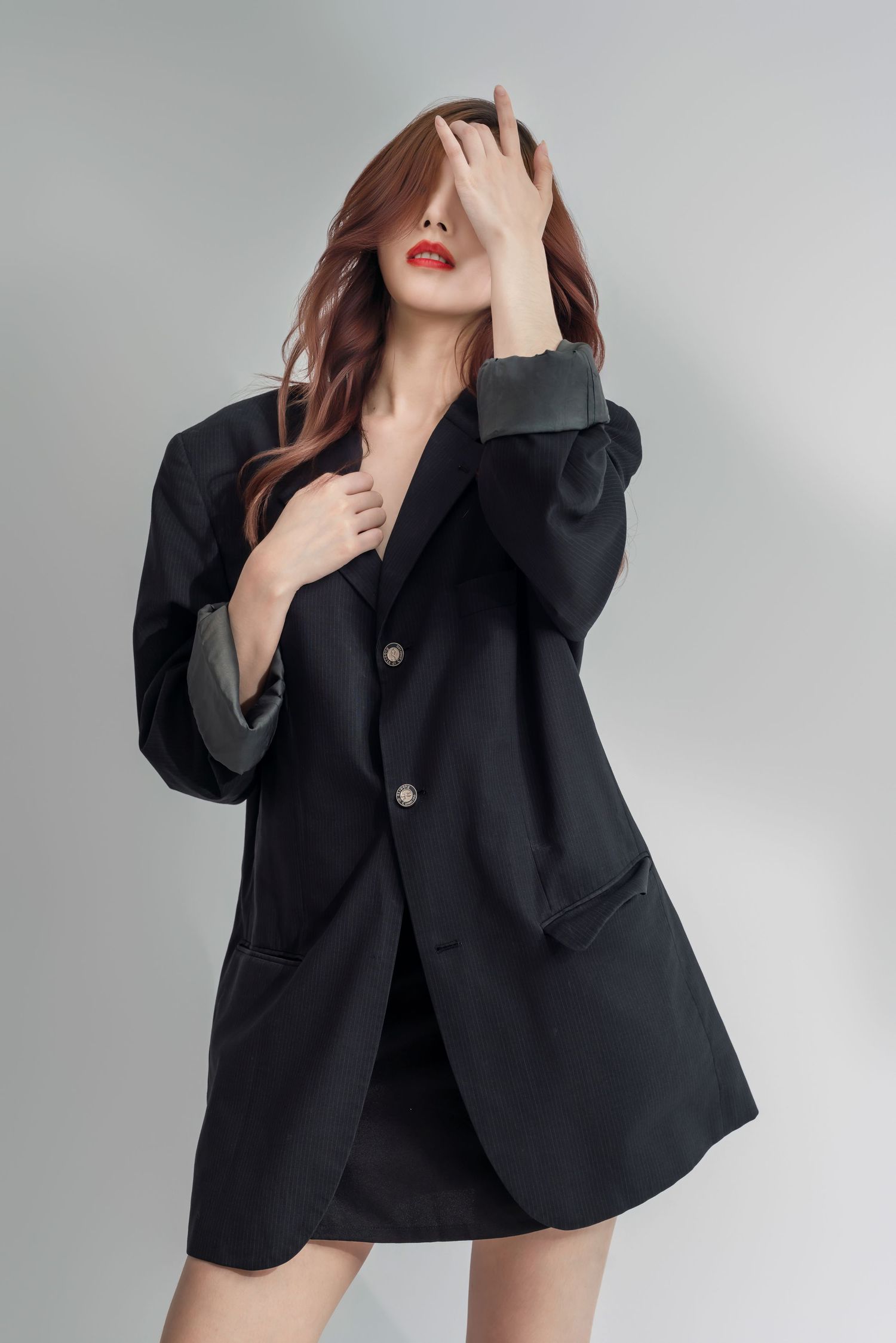 Stylish black oversized blazer jacket worn as a dress against grey background in dramatic fashion pose.