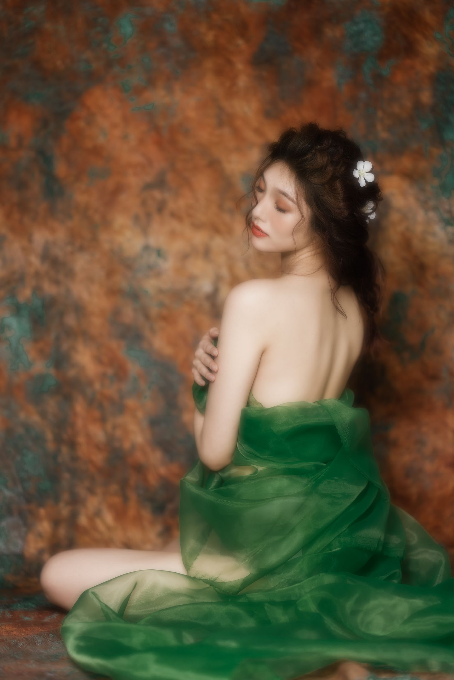 Artistic portrait of a woman in flowing emerald green fabric posing against a textured bronze and teal backdrop.