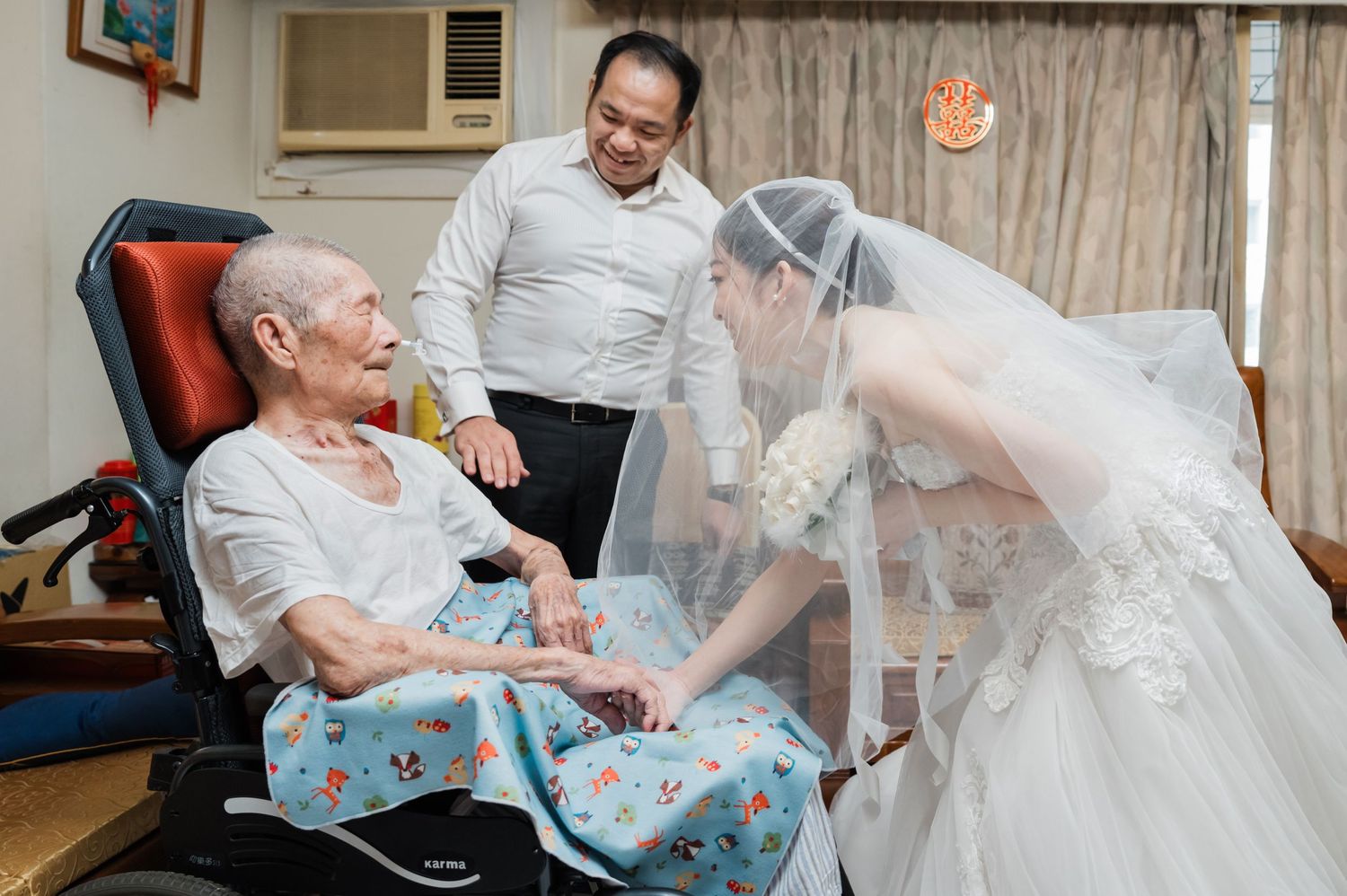 A heartwarming scene of a person in a wedding dress visiting someone seated in a medical chair while another person stands nearby.