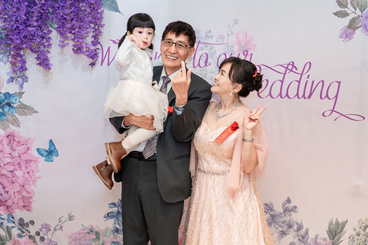 A couple celebrates their wedding day in front of a purple floral backdrop with butterflies.