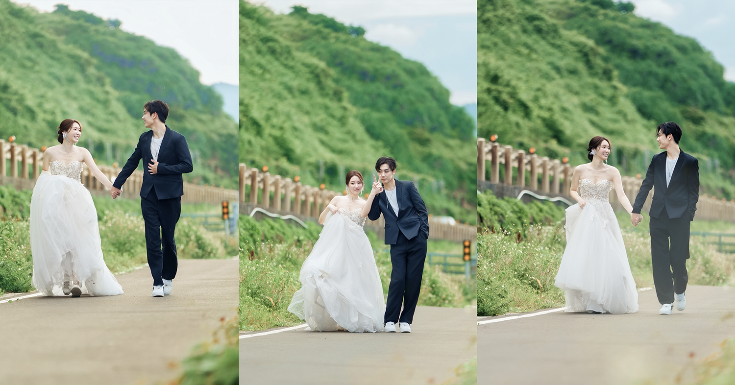 A couple walks hand in hand along a scenic coastal pathway with green hillside views on a misty day.