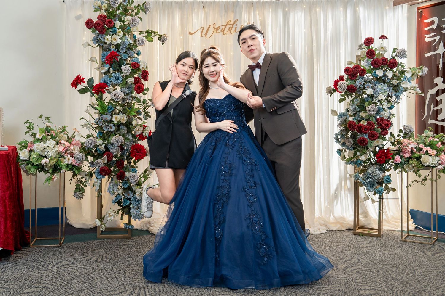 Elegant celebration scene with navy blue ballgown against white backdrop decorated with red roses and floral arrangements.